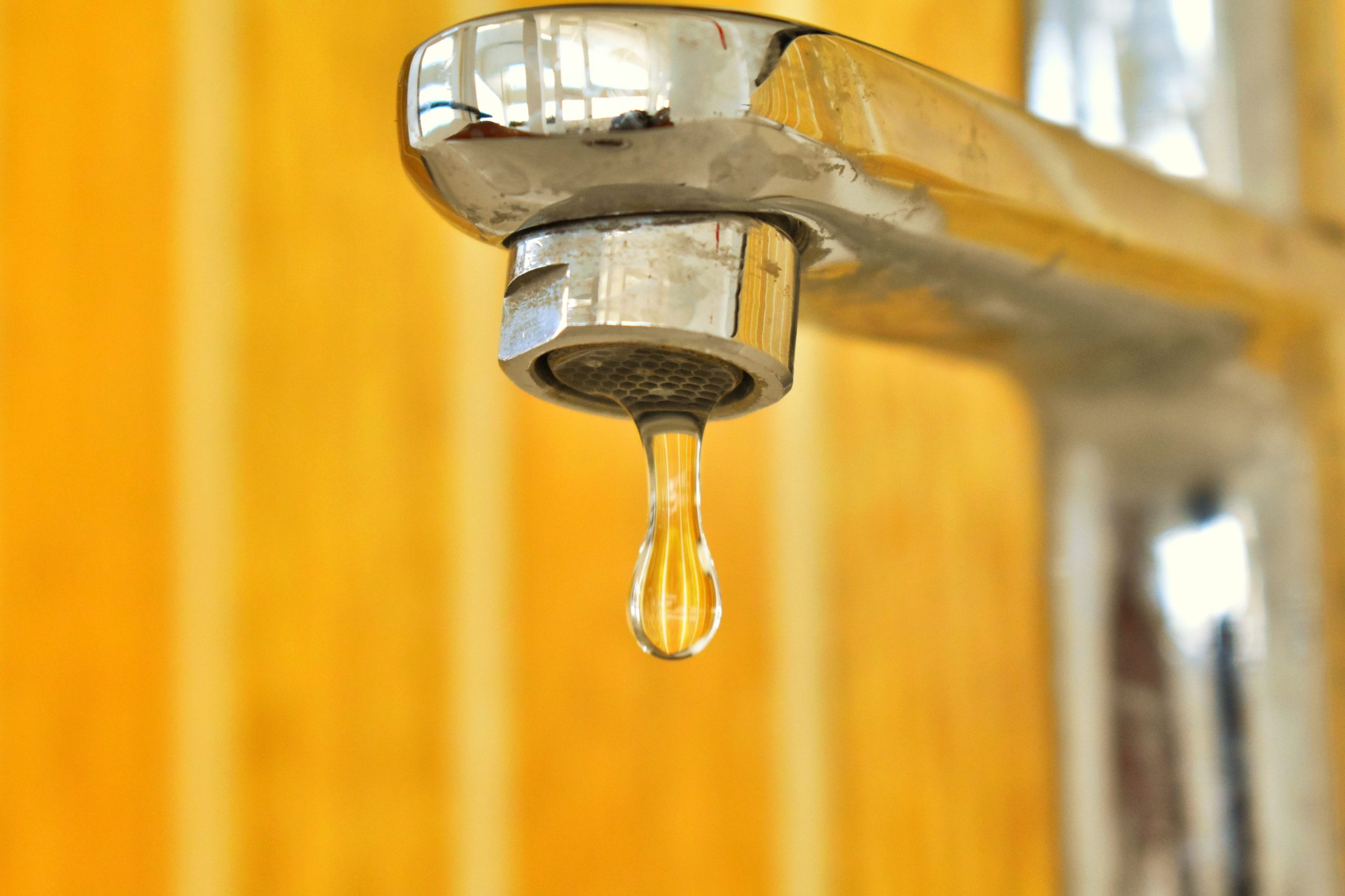 Goutte d'eau suspendue à un robinet inoxydable